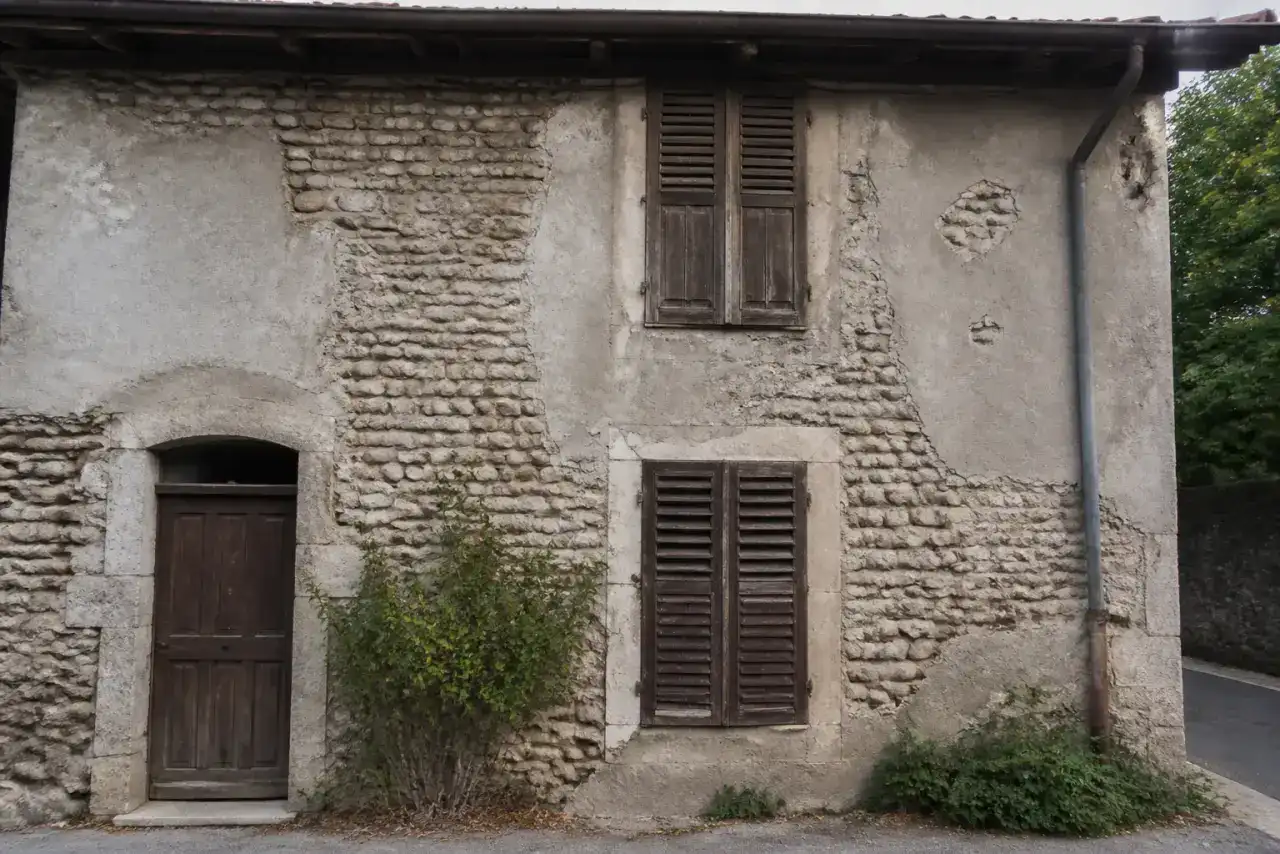 Façade de maison ancienne en galets roulés du Rhône, enduit ciment fissuré et grisâtre, photographie réaliste en lumière neutre