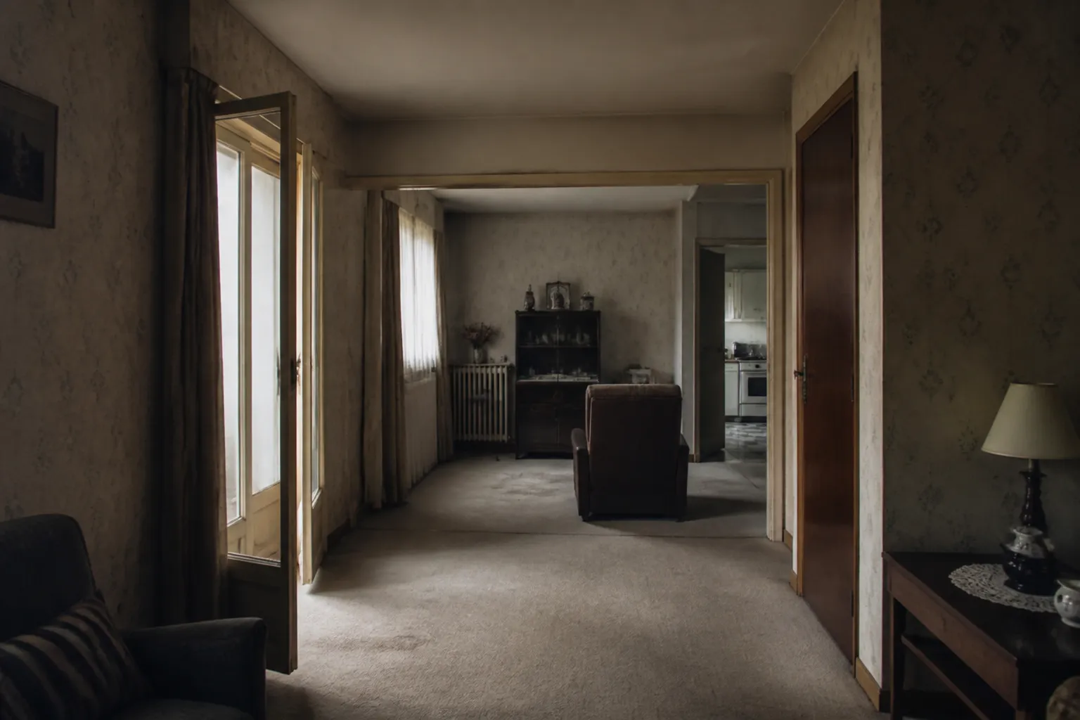 Séjour sombre et cloisonné de maison des années 70, papier peint défraîchi, moquette, lumière terne, photographie réaliste