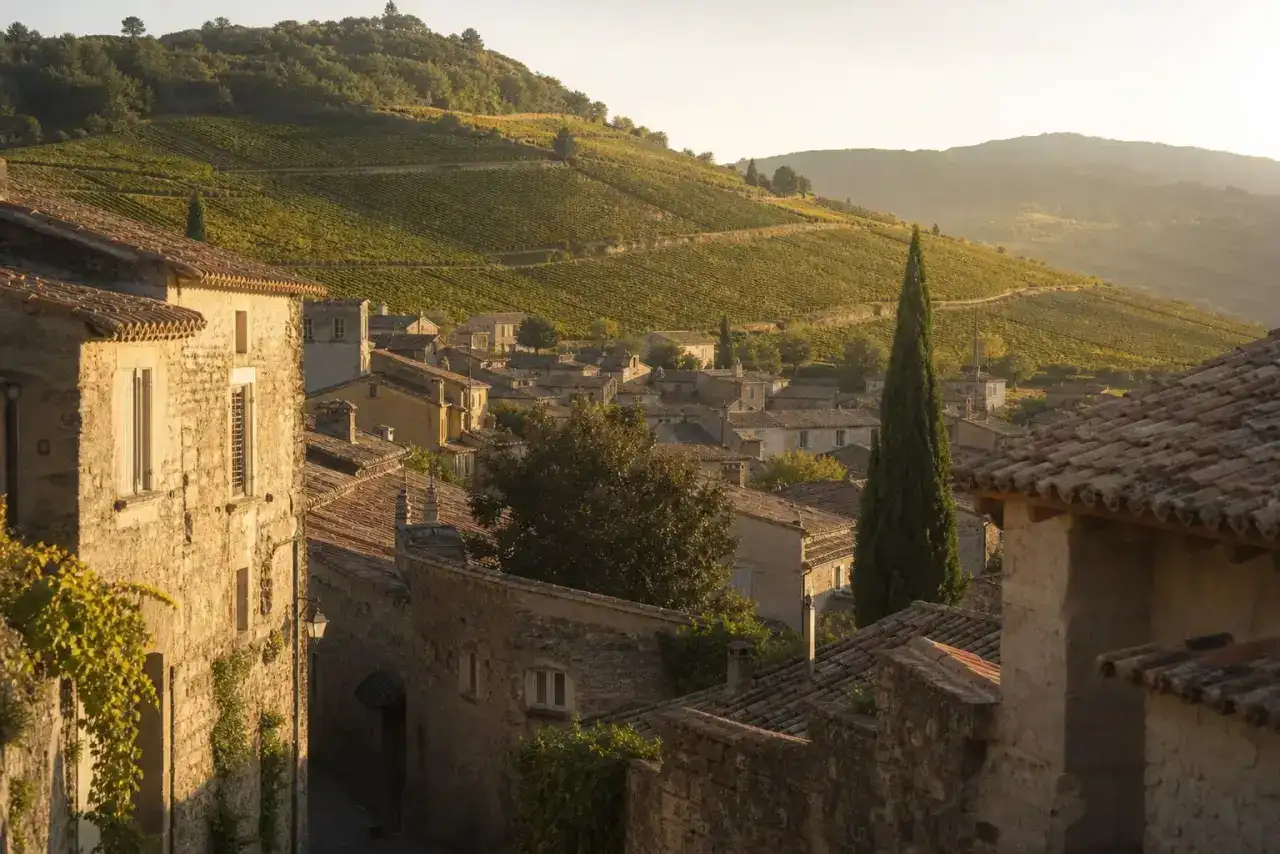 Bourg ancien au pied de coteaux plantés de vignes, maisons aux murs de pierre et toits de tuiles romanes, lumière rasante de fin d'après-midi, photographie réaliste